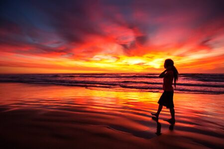 woman walking alone on the beach in the sunsetの写真素材