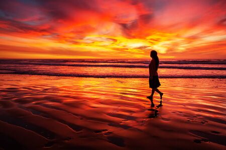 woman walking alone on the beach in the sunsetの写真素材