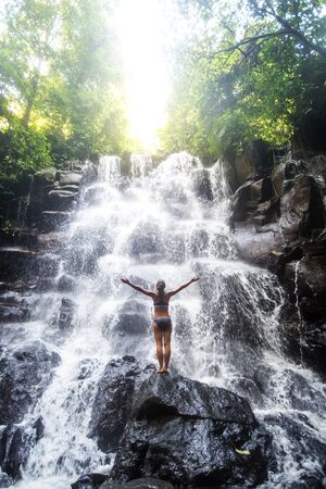 Woman practices yoga near waterfall in Bali, Indonesiaの写真素材