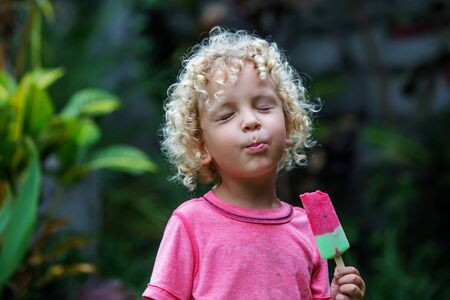 little boy with blonde curly hair is eating ice creamの写真素材