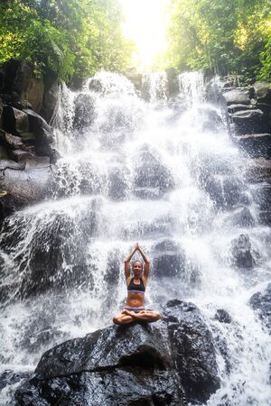 Woman practices yoga near waterfall in Bali, Indonesiaの写真素材