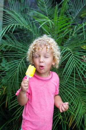little boy with blonde curly hair is eating ice creamの写真素材