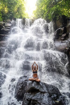 Woman practices yoga near waterfall in Bali, Indonesiaの写真素材
