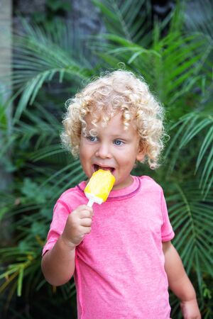 little boy with blonde curly hair is eating ice creamの写真素材