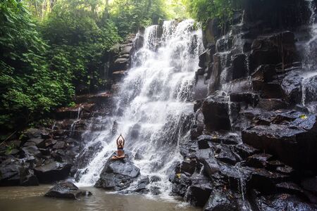 Woman practices yoga near waterfall in Bali, Indonesiaの写真素材