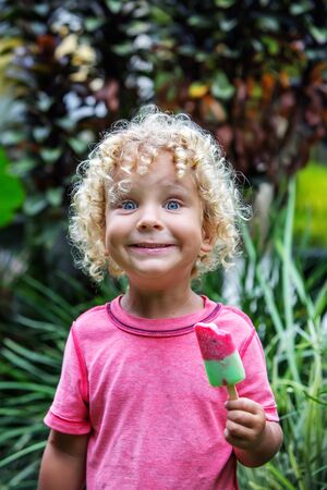 little boy with blonde curly hair is eating ice creamの写真素材