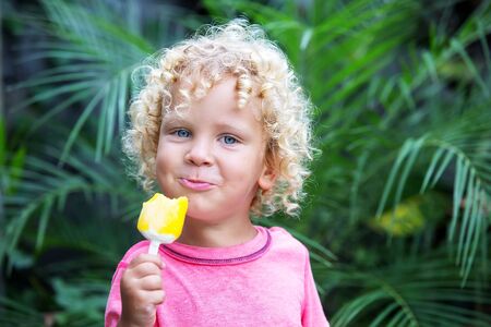 little boy with blonde curly hair is eating ice creamの写真素材