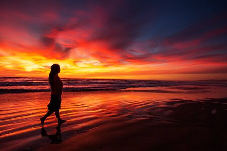 woman walking alone on the beach in the sunsetの写真素材