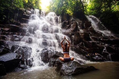 Woman practices yoga near waterfall in Bali, Indonesiaの写真素材