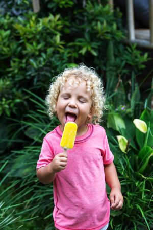 little boy with blonde curly hair is eating ice creamの写真素材