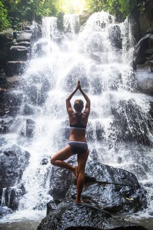Woman practices yoga near waterfall in Bali, Indonesiaの写真素材