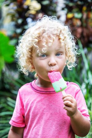 little boy with blonde curly hair is eating ice creamの写真素材