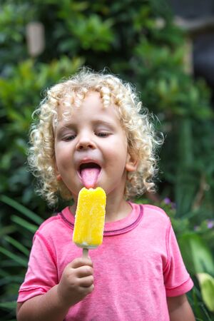 little boy with blonde curly hair is eating ice creamの写真素材