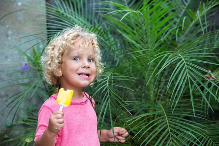 little boy with blonde curly hair is eating ice creamの写真素材