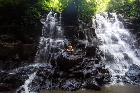 Woman practices yoga near waterfall in Bali, Indonesiaの写真素材