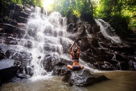 Woman practices yoga near waterfall in Bali, Indonesiaの写真素材