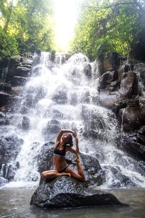 Woman practices yoga near waterfall in Bali, Indonesiaの写真素材