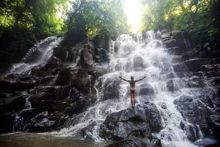 Woman practices yoga near waterfall in Bali, Indonesiaの写真素材