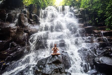 Woman practices yoga near waterfall in Bali, Indonesiaの写真素材