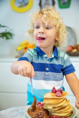 Little curly boy eating sweet pancakesの写真素材