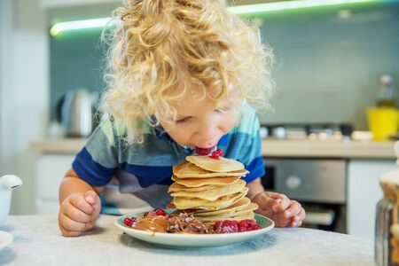 Little curly boy eating sweet pancakesの写真素材