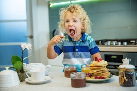 Little curly boy eating sweet pancakesの写真素材
