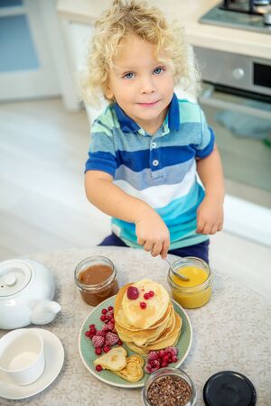 Little curly boy eating sweet pancakesの写真素材