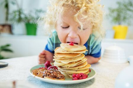 Little curly boy eating sweet pancakesの写真素材