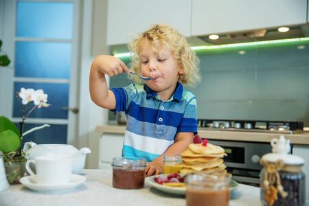 Little curly boy eating sweet pancakesの写真素材
