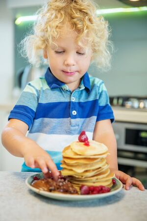 Little curly boy eating sweet pancakesの写真素材