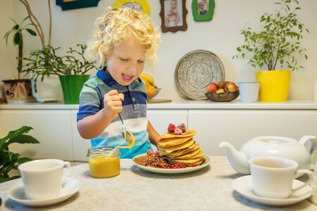 Little curly boy eating sweet pancakesの写真素材