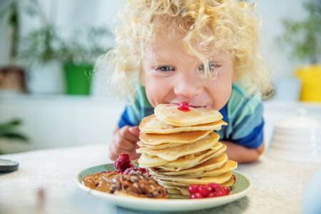 Little curly boy eating sweet pancakesの写真素材