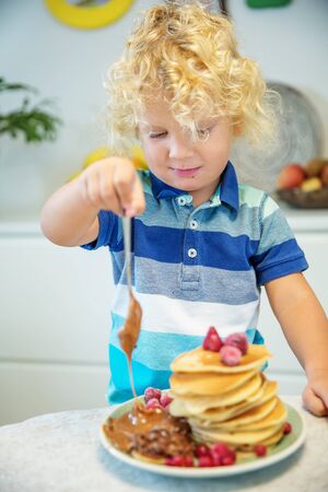 Little curly boy eating sweet pancakesの写真素材
