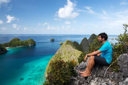 Tourists are on the top of the cliff of remote archipelago Pulau Wayag, Raja Ampat, Indonesiaの写真素材