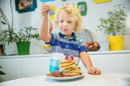 Little curly boy eating sweet pancakesの写真素材
