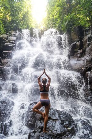 Woman practices yoga near waterfall in Bali, Indonesiaの写真素材