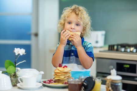 Little curly boy eating sweet pancakesの写真素材