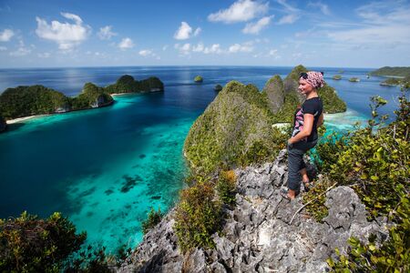 Tourists are on the top of the cliff of remote archipelago Pulau Wayag, Raja Ampat, Indonesiaの写真素材