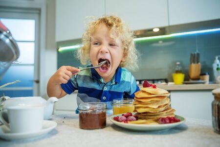 Little curly boy eating sweet pancakesの写真素材