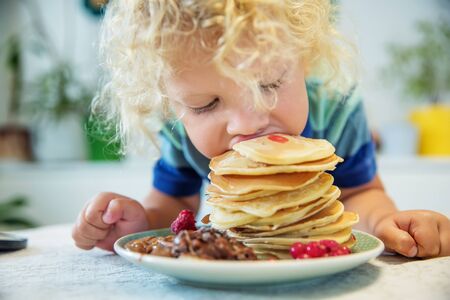 Little curly boy eating sweet pancakesの写真素材