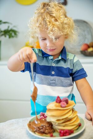 Little curly boy eating sweet pancakesの写真素材