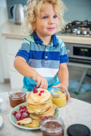 Little curly boy eating sweet pancakesの写真素材