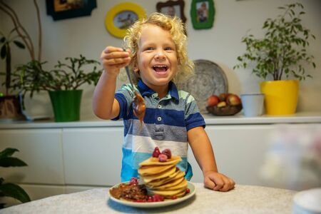 Little curly boy eating sweet pancakesの写真素材