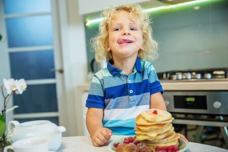 Little curly boy eating sweet pancakesの写真素材