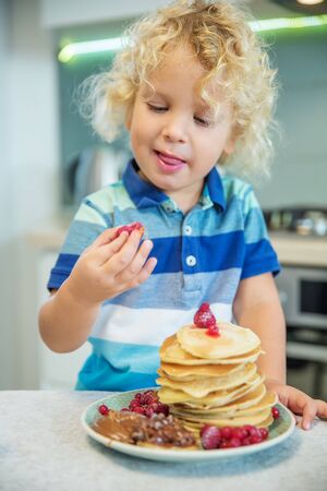 Little curly boy eating sweet pancakesの写真素材