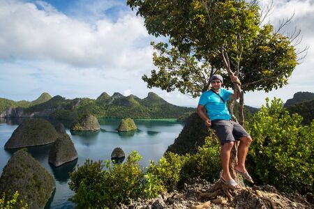 Tourists are on the top of the cliff of remote archipelago Pulau Wayag, Raja Ampat, Indonesiaの写真素材
