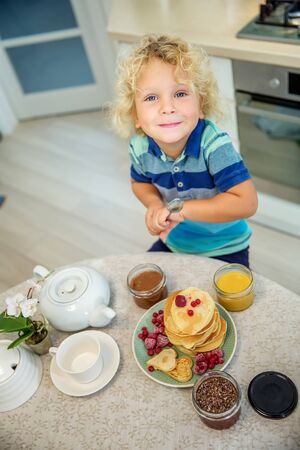 Little curly boy eating sweet pancakesの写真素材