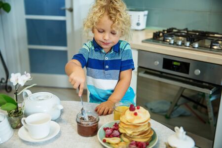 Little curly boy eating sweet pancakesの写真素材