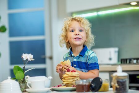 Little curly boy eating sweet pancakesの写真素材