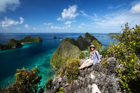 Tourists are on the top of the cliff of remote archipelago Pulau Wayag, Raja Ampat, Indonesiaの写真素材